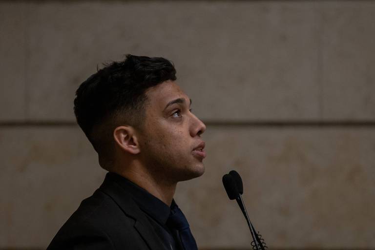 Vestido de preto, Gabriel Monteiro olha pra cima enquanto fala no microfone à sua frente na Câmara de Vereadores do Rio