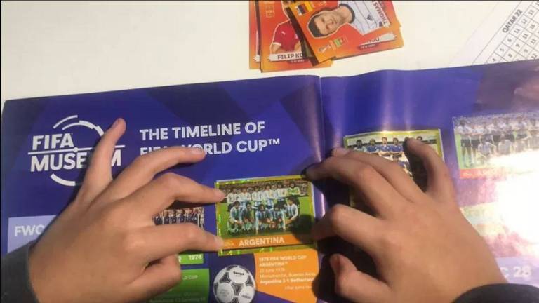 Menino cola uma figurinha da seleção argentina de futebol no álbum da Copa do Qatar-2022