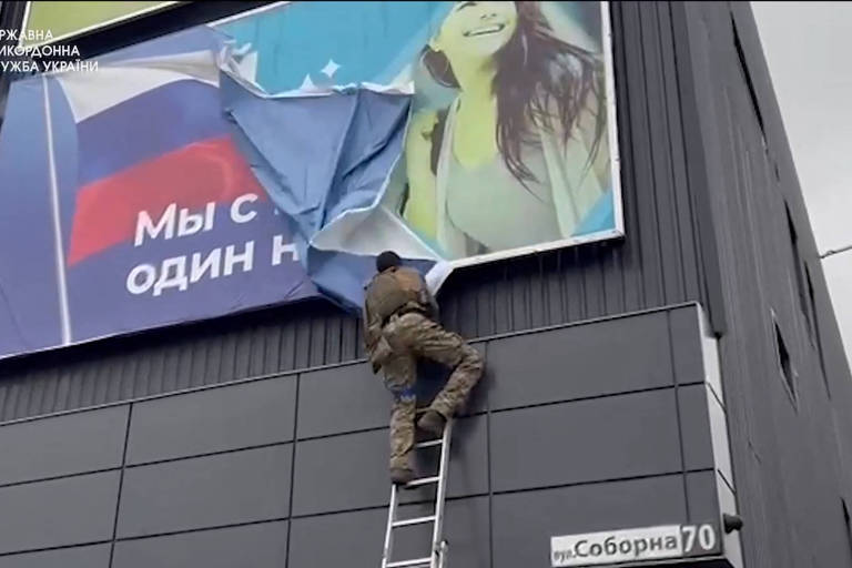 Soldado ucraniano arranca cartaz de propaganda russa em Vovtchansk, retomada por Kiev na região de Kharkiv, em vídeo divulgado pelo governo