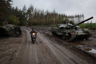 A local resident rides at a scooter near a destroyed Russian tank in the town of Izium