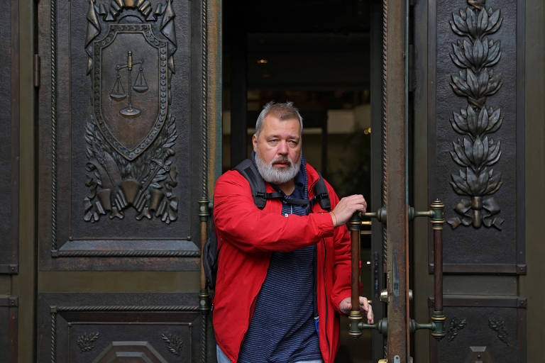 Homem vestindo casaco vermelho passa pela porta de entrada de um prédio