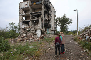 Women stand near a residential building destroyed by a military strike in the town of Izium