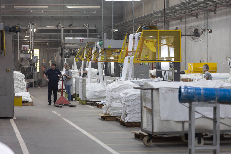 Imagem mostra trabalhador em linha de produção perto de algumas máquinas.