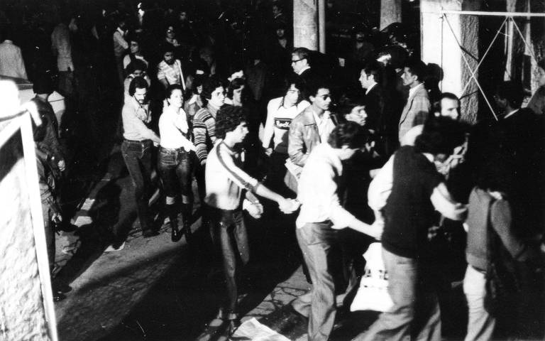 Estudantes detidos são conduzidos em fila indiana e de mãos dadas ao estacionamento durante ação da repressão da PUC