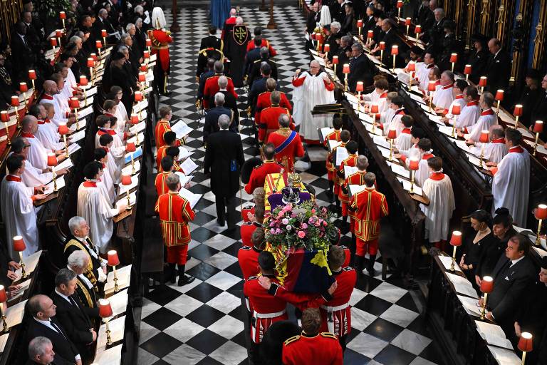 O caixão da Rainha Elizabeth II, envolto em um Estandarte Real e adornado com a Coroa Imperial do Estado e o orbe e cetro do Soberano; o funeral acontece na abadia de Westminster, em Londres