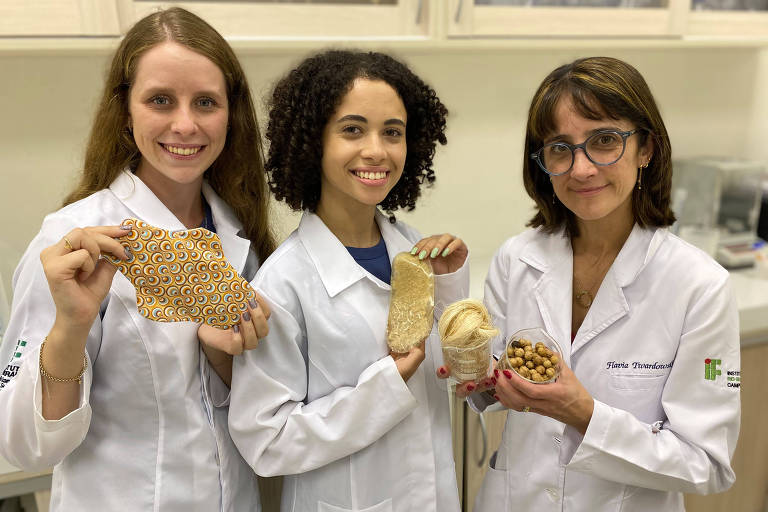 Três mulheres de jaleco seguram protótipo de absorvente sustentável que elas desenvolveram