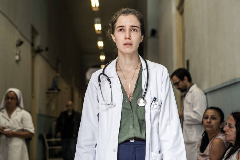 Em foto colorida, mulher de uniforme de médica posta em frente ao hospital