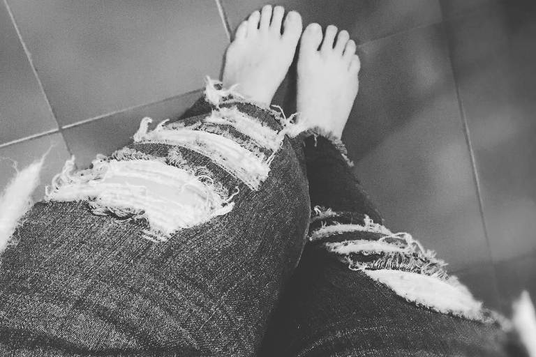 Foto mostra duas pernas vestindo uma calça jeans rasgada
