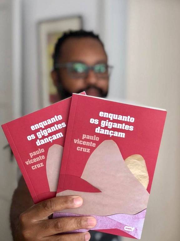 Paulo Vicente Cruz estende duas cópias do seu livro, "Enquanto os gigantes dançam"