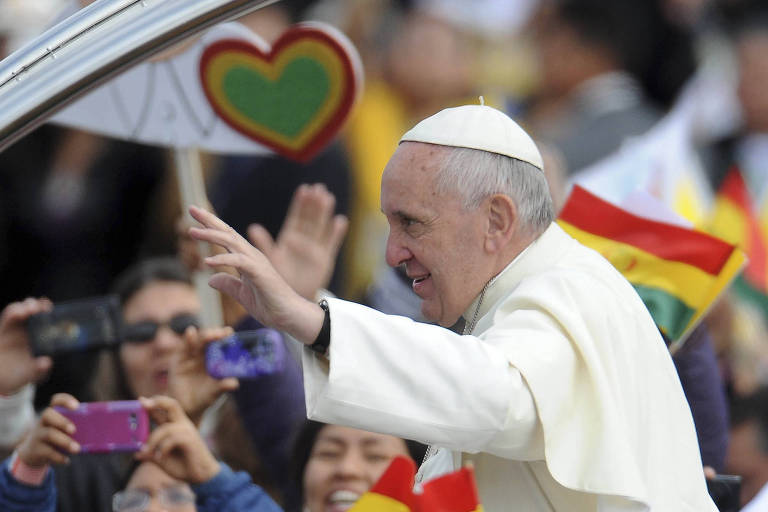 Papa Francisco está de perfil e veste roupas brancas. Ao fundo, pessoas celebram sua passagem.