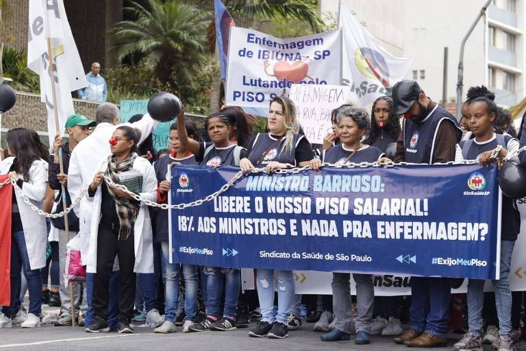 Fotografia colorida mostra um grupo de profissionais segurando cartazes, entre eles, em destaque um com a frase: "Ministro Barroso: Libere o nosso piso salarial!"
