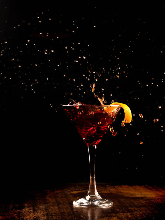 Splash shot com coquetel laranja martini no balcão de madeira com fundo escuro.