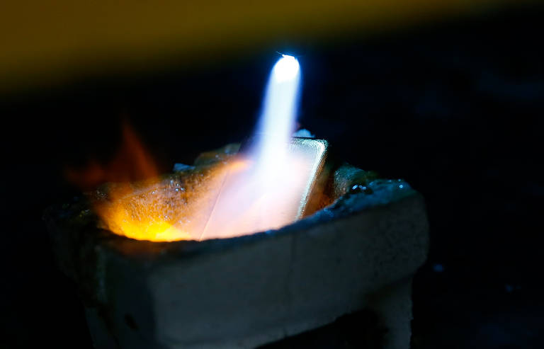 Fotografia colorida mostra uma chama saindo de um maçarico e atingindo uma barra de ouro.