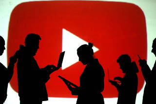 FILE PHOTO: Silhouettes of laptop and mobile device users next to a screen projection of the YouTube logo in this picture illustration