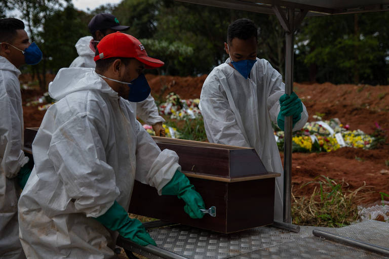 Sepultadores paramentados enterram caixão no Cemitério Vila Formosa, na capital paulista