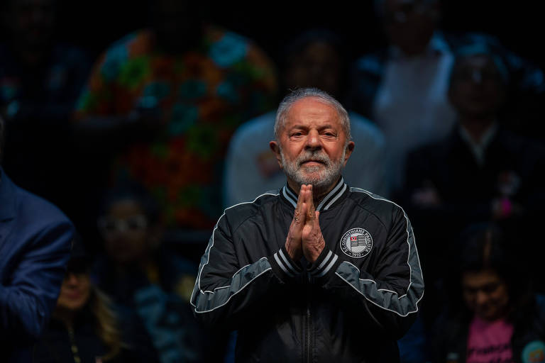 Imagem mostra Lula com as duas mãos encostadas formando o sinal de prece. Atrás dele, há vários apoiadores.