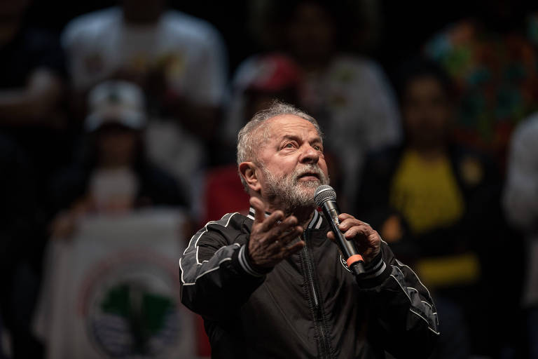 Fotografia colorida mostra o ex-presidente e candidato à eleição Luiz Inácio Lula da Silva. Ele é um homem branco de cabelo grisalho e fala ao microfone para a platéia. 
