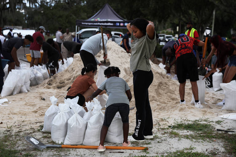 Alicia Dhall, 18, olha para baixo enquanto sua irmã Ariana, 8, e moradores locais enchem sacos de areia para prevenir inundações em Tampa, cidade do estado americano da Flórida