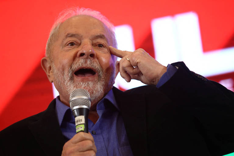 Imagem mostra Lula apontando dedo indicador para a cabeça enquanto discursa com microfone. 