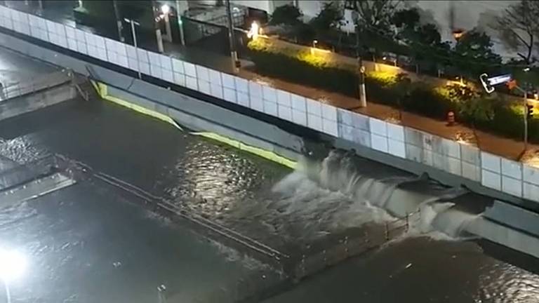 Foto mostrando inundação em canteiro de obras. A água invade e derruba um muro do canteiro à direita.
