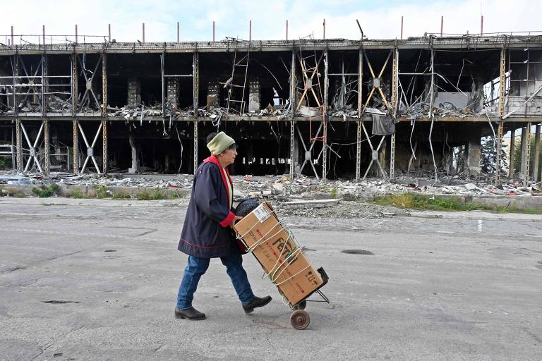 Moradora de Izium, cidade de Kharkiv que foi retomada pelos ucranianos, passa por prédio destruído
