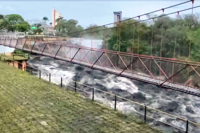 Imagem do rio Tietê, embaixo de uma ponte, com a água preta.