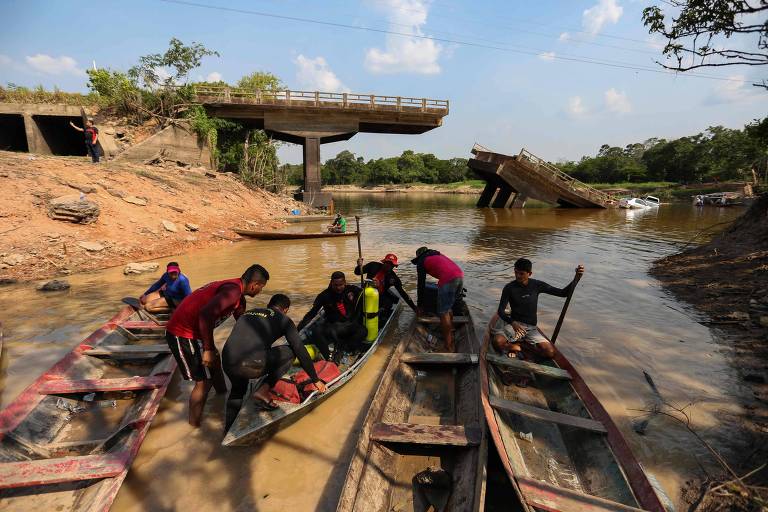 Pessoas se posicionam em canoas, com a ponte ruída ao fundo