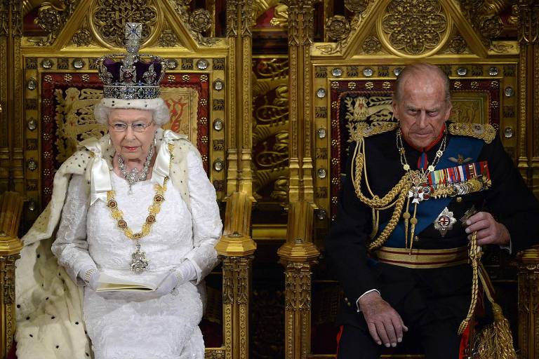 Rainha Elizabeth 2ª e o Príncipe Philip sentados, um ao lado do outro, em seus tronos.