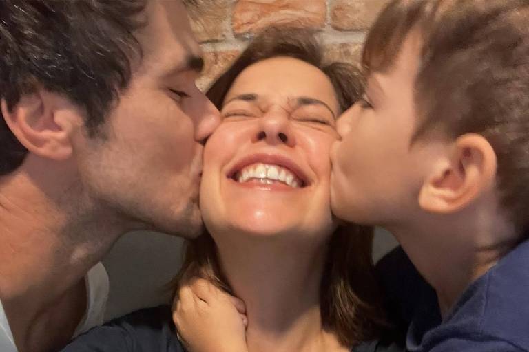 Mulher recebendo beijo na bochecha de um homem e uma criança