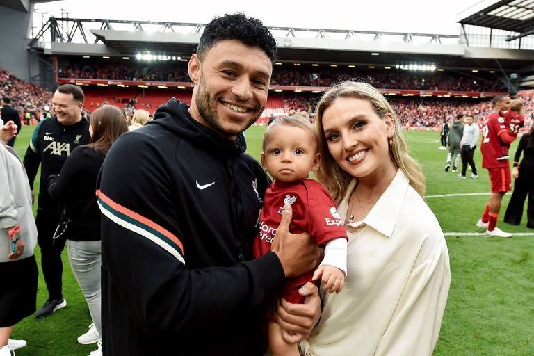 Casal hétero posando para foto com bebê no colo em um campo de futebol