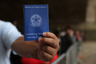 A man shows his work permit (employment record card) as he lines up to fill out applications while looking for job opportunities in downtown Sao Paulo