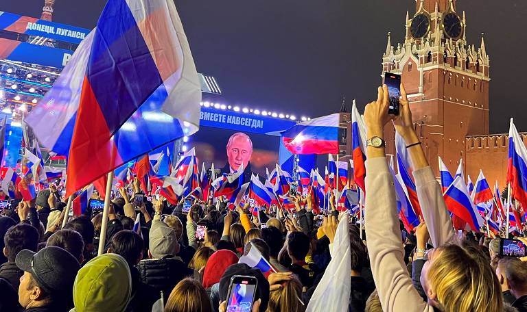 Russos erguem bandeiras nacionais durante declaração de Vladimir Putin sobre a anexação de territórios da Ucrânia, na praça Vermelha, centro de Moscou 