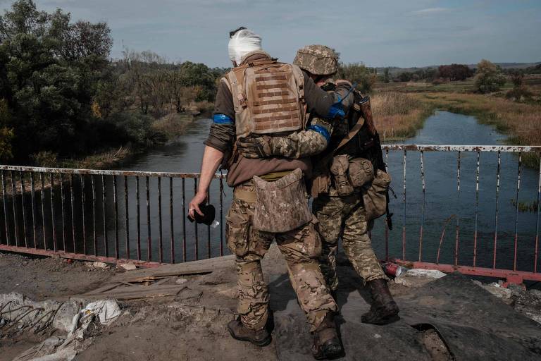 Soldado ucraniano apoia colega ferido ao cruzar ponte sobre o rio Oskil, em área retomada por Kiev em Kharkiv