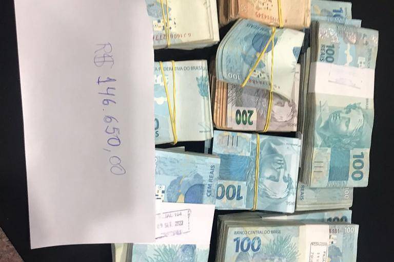 Foto colorida mostra notas de dinheiro. Um papel branco escrito a caneta mostra o número de 146 mil reais