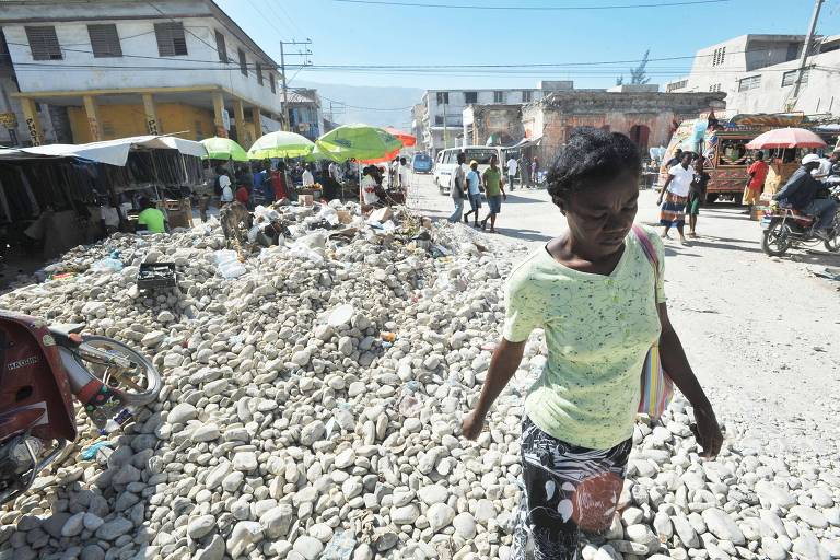 Mulher anda por rua de terra, com escombros do lado, na capital do Haiti