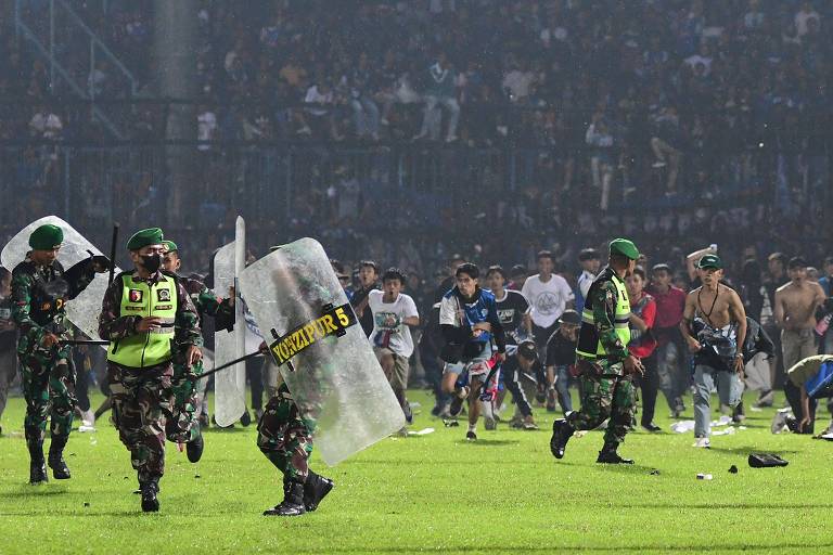 Torcedores correm pelo gramado próximos a oficiais da polícia durante confusão em partida de futebol na Indonésia