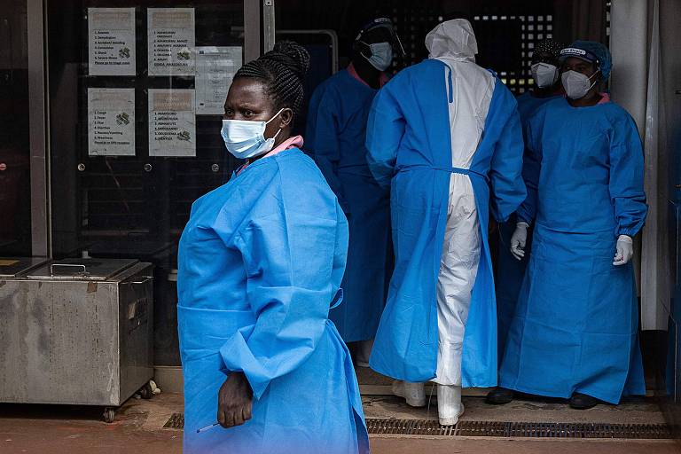Enfermeiros na porta de hospital em Uganda. Todos são negros e estão protegidos com máscara, luvas cirúrgicas e uma capa azul.