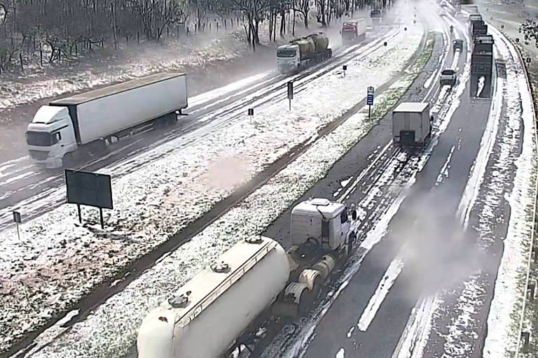 foto de câmera de trânsito mostra veículos em rodovia que tem grandes porções com gelo após chuva de granizo 