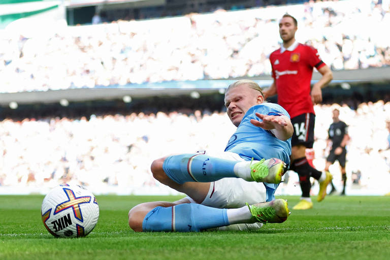 Haaland atira-se no gramado para conseguir acertar a bola, que está à sua frente, e marcar gol pelo Manchester City na goleada sobre o Manchester United no Campeonato Inglês