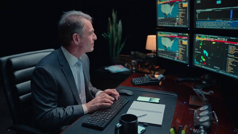 Um homem de cabelo grisalho mexe em um computador com várias telas.