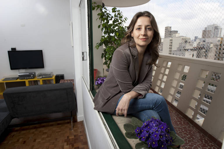 A arquiteta Simone Gatti na janela do seu apartamento, com a vista de São Paulo ao fundo