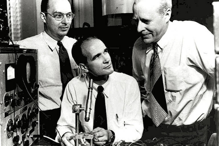 Prêmio Nobel de Física de 1956, John Bardeen [à esq.] com William Shockley [sentado] e Walter Brattain no Laboratório Bell Laboratory, em 1947