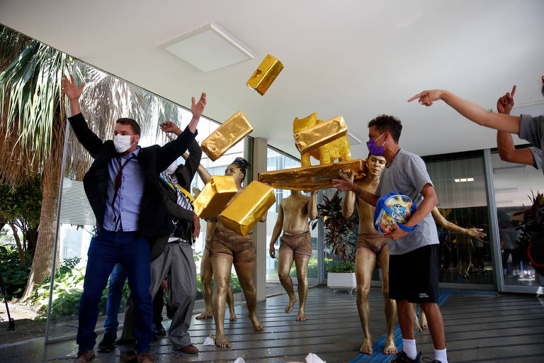 manifestantes jogam barras de ouro falsas para o alto, na porta do MEC. Há seis pessoas, uma delas de terno, e outras fantasiadas