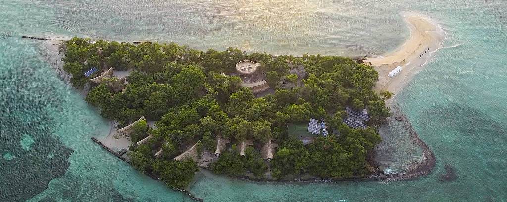 Fotografia colorida com vista aérea da ilha Corona, com árvores e mar