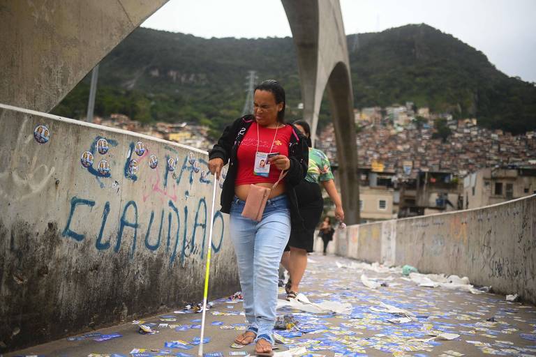 Mulher caminha sobre passarela. Favela ao fundo.