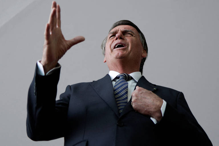 Imagem mostra o presidente Jair Bolsonaro, em entrevista concedida no Palácio do Alvorada. Ele é um homem branco, que veste um terno escuro e camisa branca, com gravata azul. Ele gesticula, enquanto fala