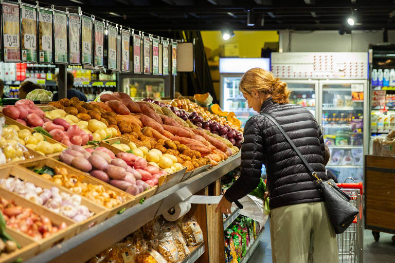 Mulher loira de blusa de frio preta e calça clara de costas, escolhendo alimentos em um supermercado em Sidney, na Austrália 