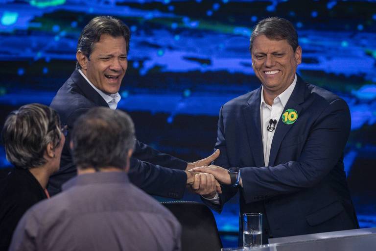 Candidatos Fernando Haddad (PT) e Tarcísio de Freitas (Republicanos) dão as mãos durante intervalo do debate promovido pela TV Bandeirantes; os dois estão sorrindo em clima amistoso 