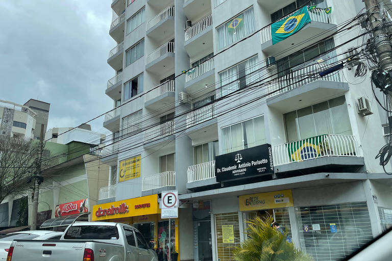 Imagem mostra a fachada de um prédio com três bandeiras do Brasil em diferentes apartamentos.