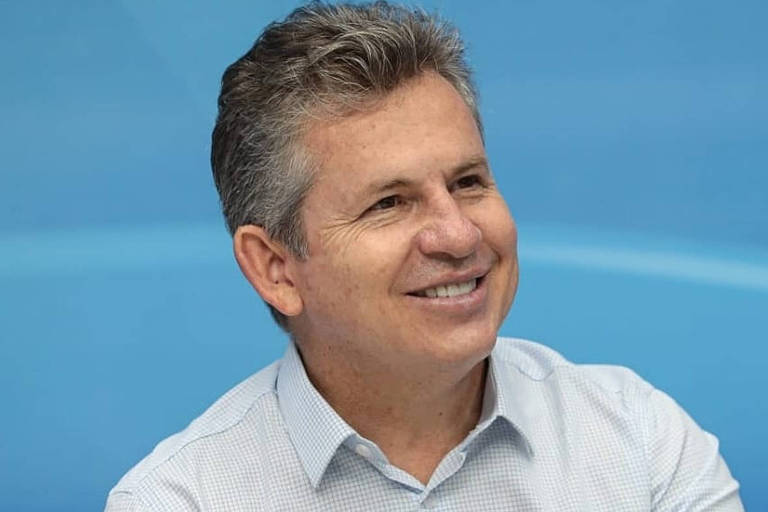 Imagem mostra o governador de Mato Grosso, Mauro Mendes (União Brasil), que foi reeleito no primeiro turno; ele usa uma camisa clara, com fundo azul e está sorrindo